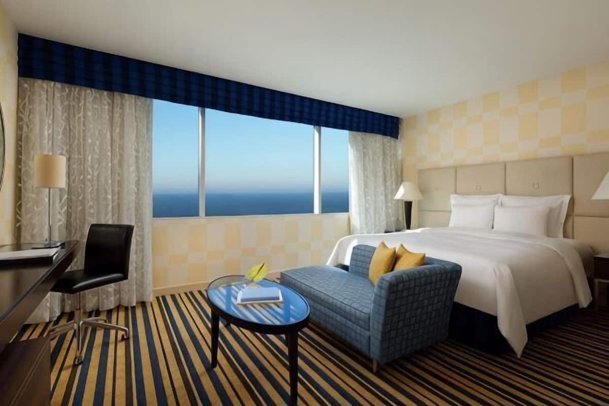 Ein Hotelzimmer mit Bett, Schreibtisch, Stuhl, einem kleinen Tisch und Meerblick.
