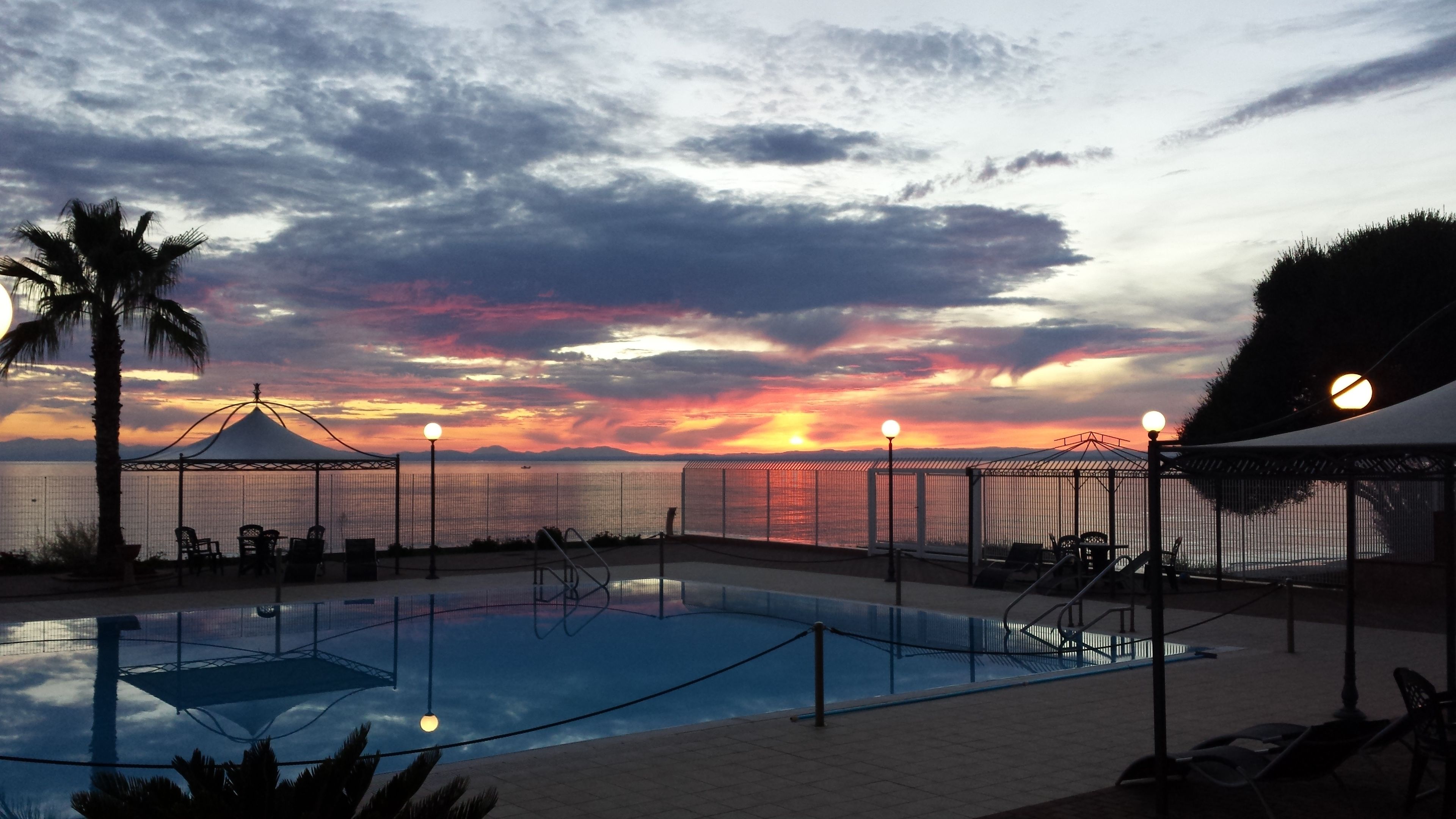 A swimming pool with a sunset view, surrounded by lounge chairs and a fence.