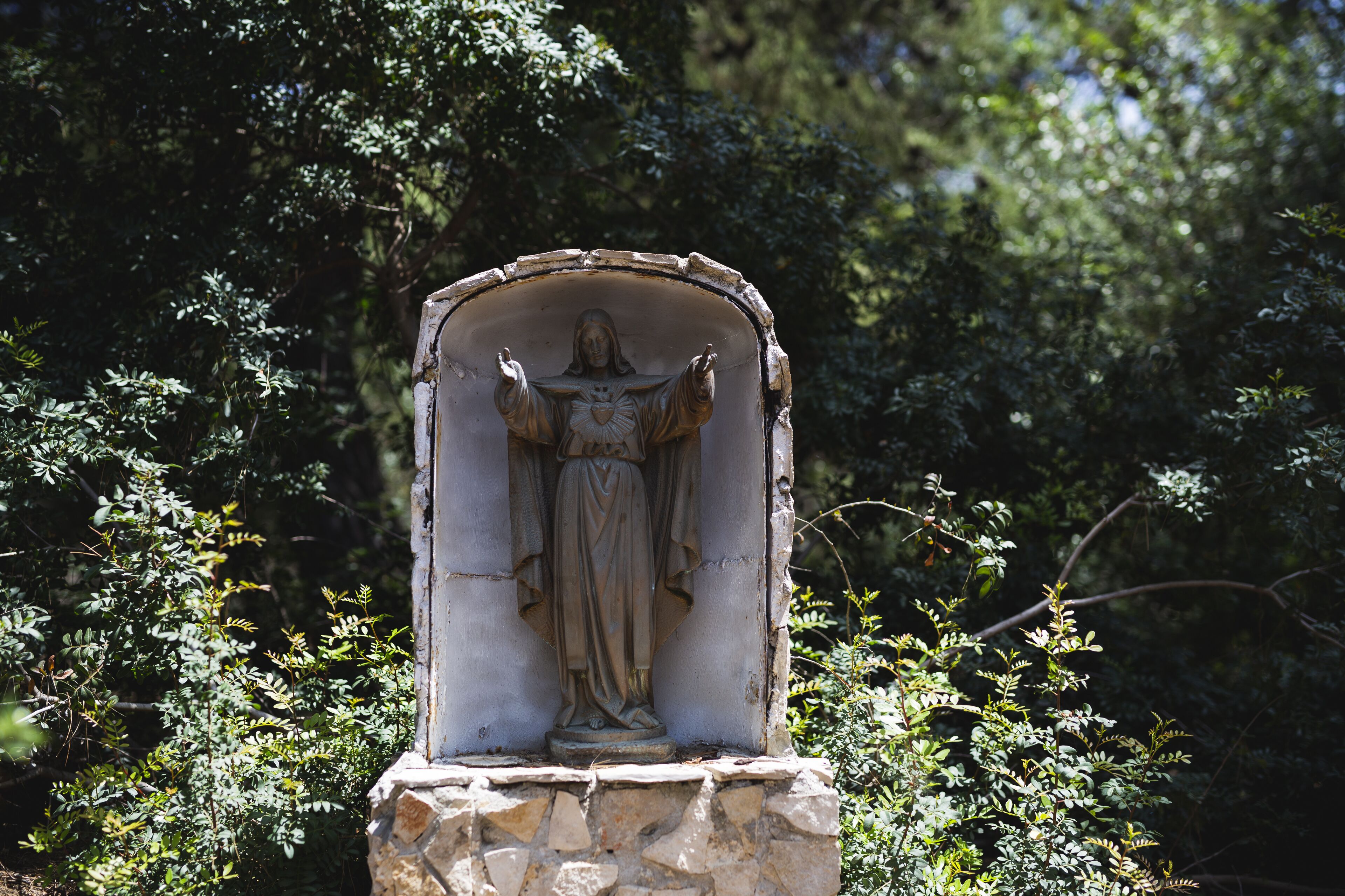 Una estatua de piedra de una figura con los brazos extendidos, ubicada en un nicho rodeado de follaje.