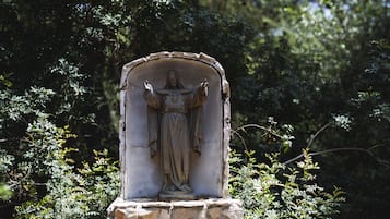 Una estatua de piedra de una figura con los brazos extendidos, ubicada en un nicho rodeado de follaje.