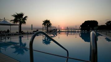 A swimming pool with a clear view of the sunset, palm trees, and a covered seating area.