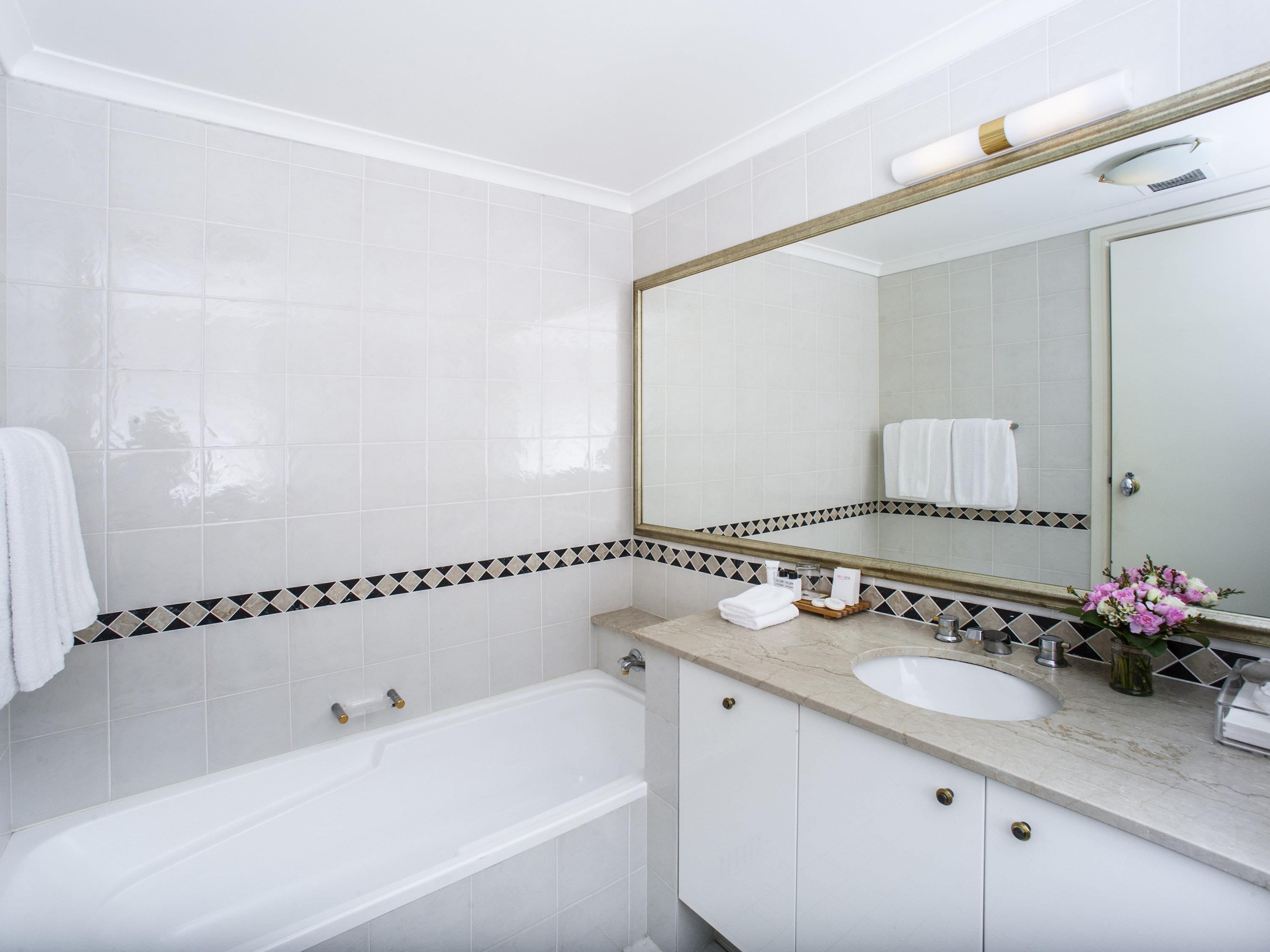 A modern bathroom with a bathtub, a sink, a mirror, and a vanity with toiletries.