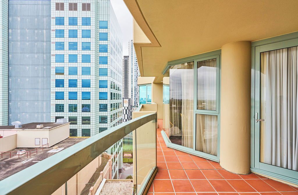Un balcone con pavimento piastrellato, una porta vetrata e vista su edifici alti.