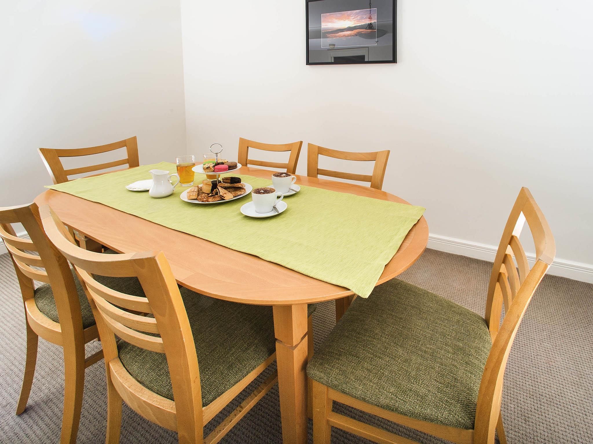 Una mesa de comedor con mantel verde, rodeada de sillas de madera con cojines verdes.