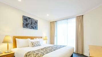 Ein Hotelzimmer mit einem großen Bett, zwei Nachttischlampen, einem Telefon, einem Schreibtisch und einem fenster mit Vorhängen.