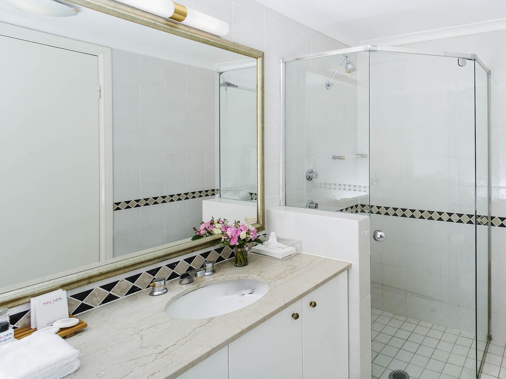 A modern bathroom with a white sink, a large mirror, and a glass-enclosed shower.