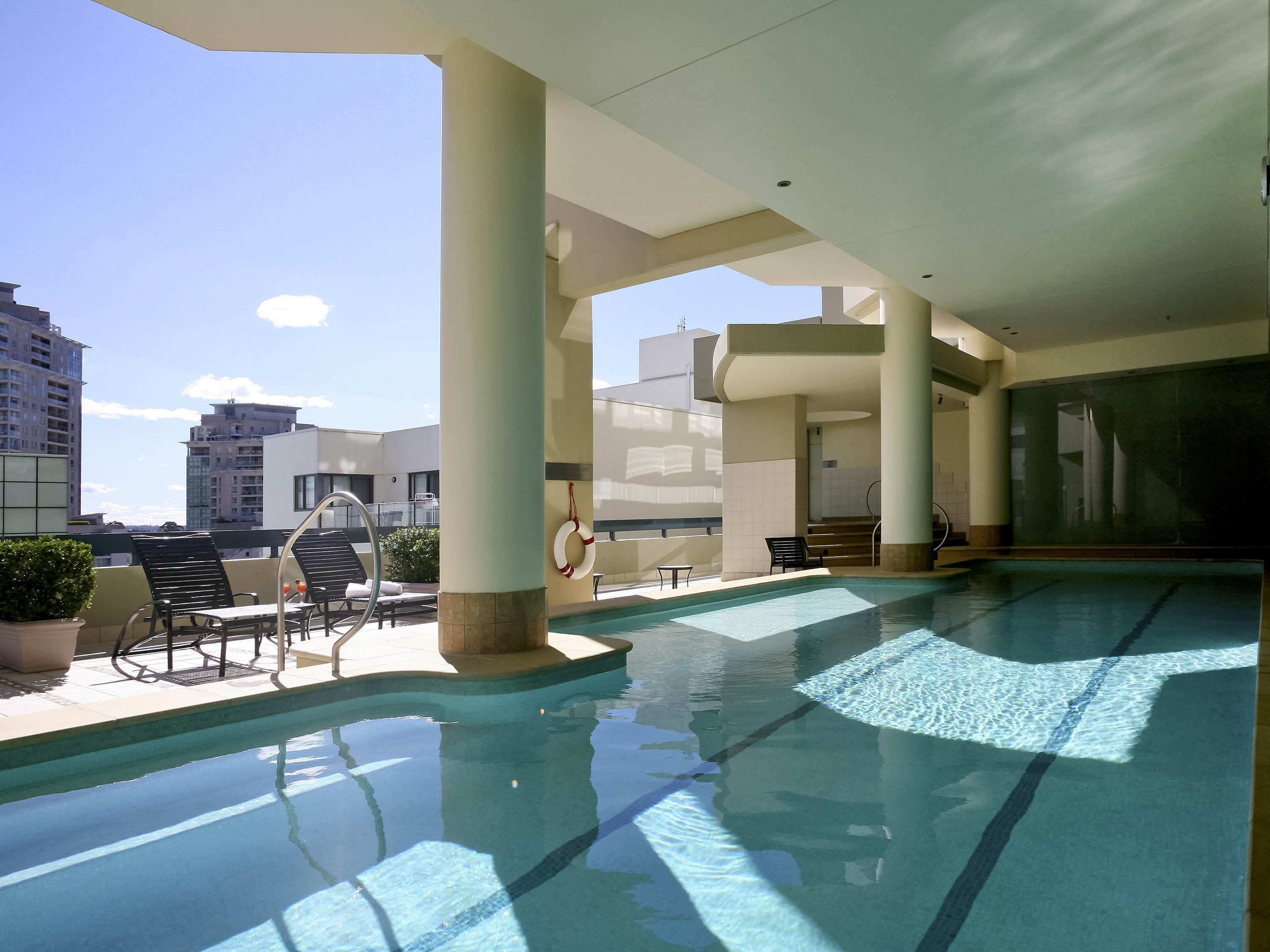 A rooftop pool with clear blue water, surrounded by lounge chairs and a lifebuoy.