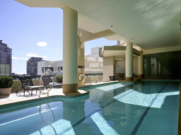 Una piscina en la azotea con agua cristalina y azul, rodeada de sillones de descanso y un flotador.