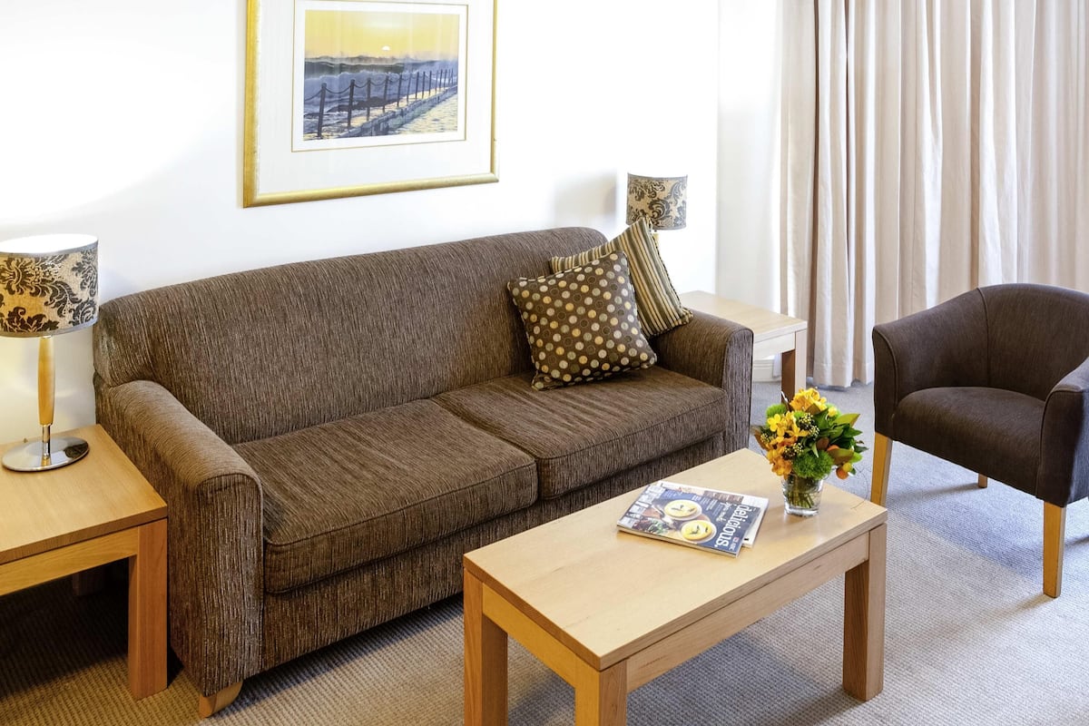 A living room with a brown sofa, a wooden coffee table, a framed picture on the wall, and a chair.