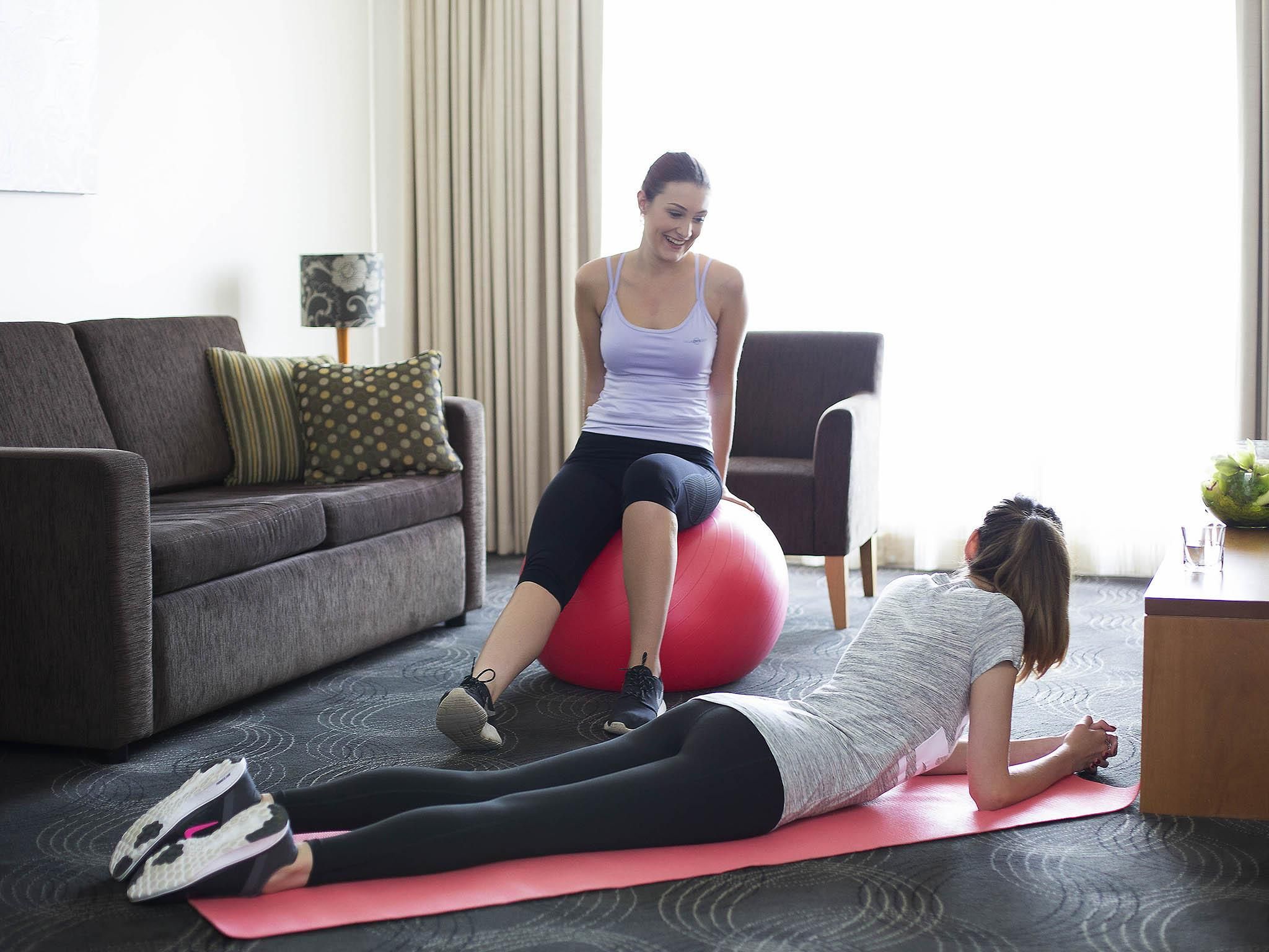 Ein Zimmer mit einer Couch, einem Sessel, einer Yogamatte und einem großen Gymnastikball.