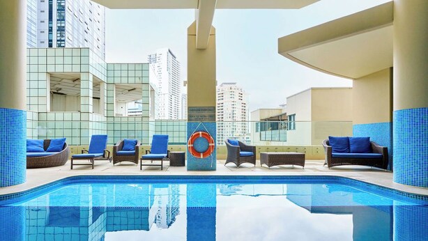 Un área de piscina en la azotea con sillones de descanso y un flotador salvavidas, rodeada de edificios altos.