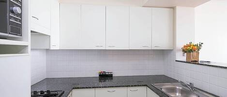 A modern kitchen with white cabinets, a gas stove, a sink, and a countertop.