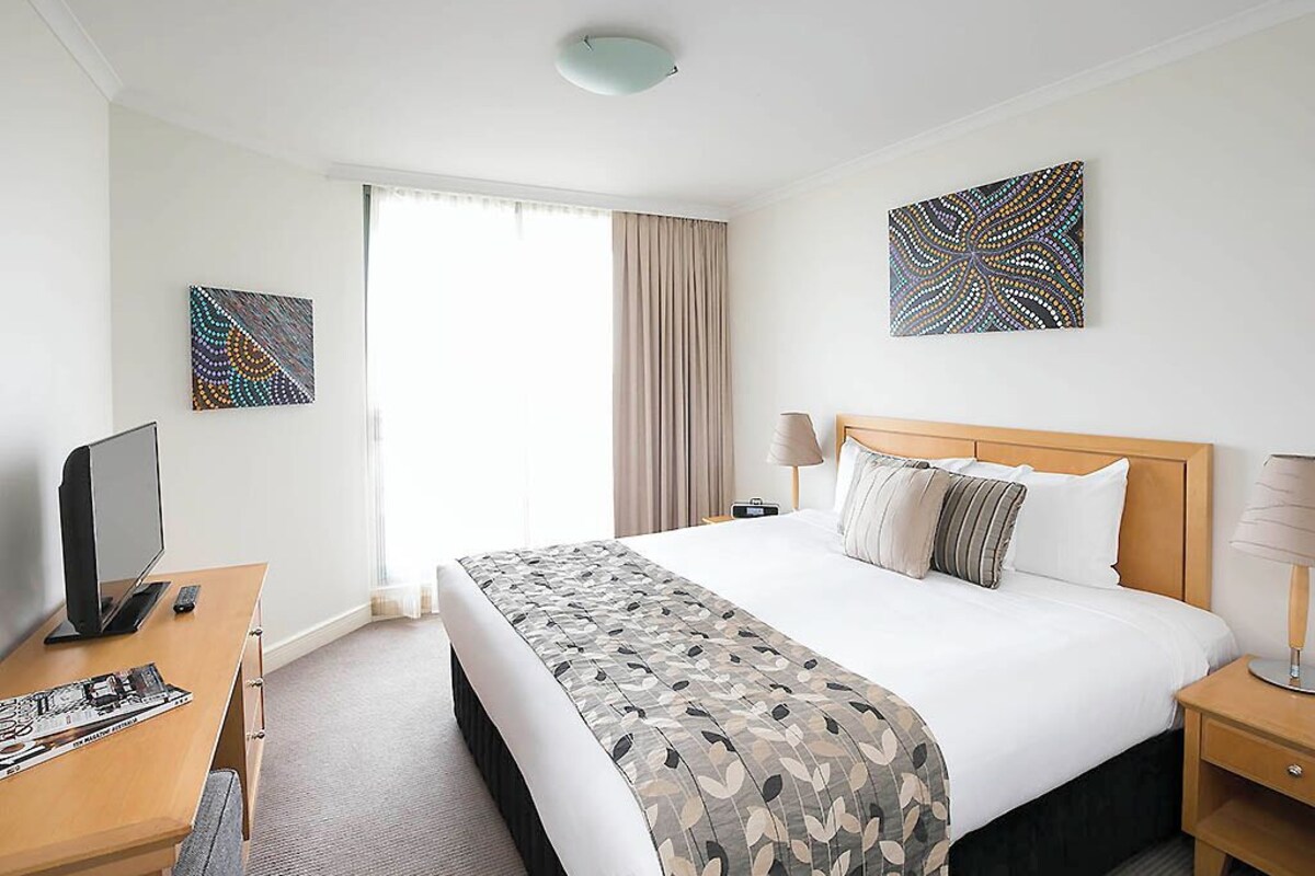 A hotel room with a large bed, a desk with a computer, a lamp, and artwork on the walls.