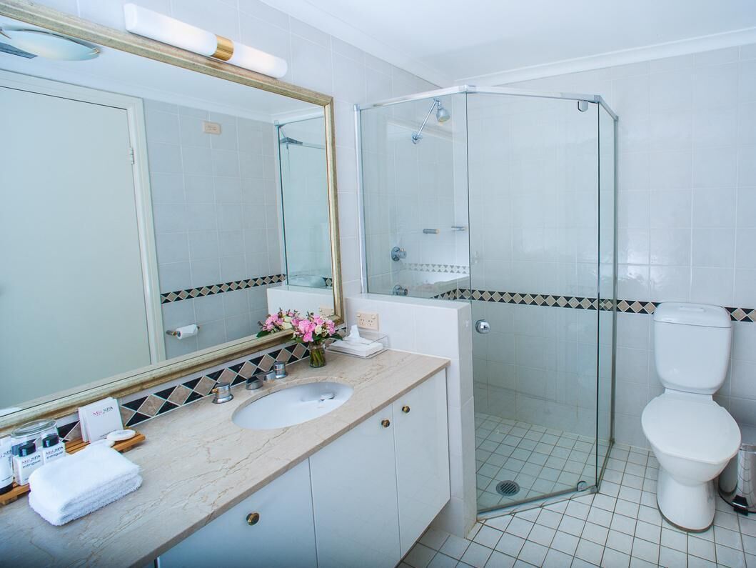 A bathroom with a glass-enclosed shower, a white toilet, and a sink with a mirror above it.