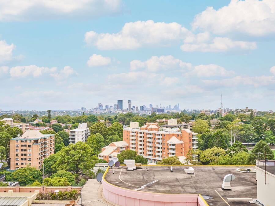 Zona residencial con edificios de apartamentos, un estacionamiento y un horizonte urbano lejano.