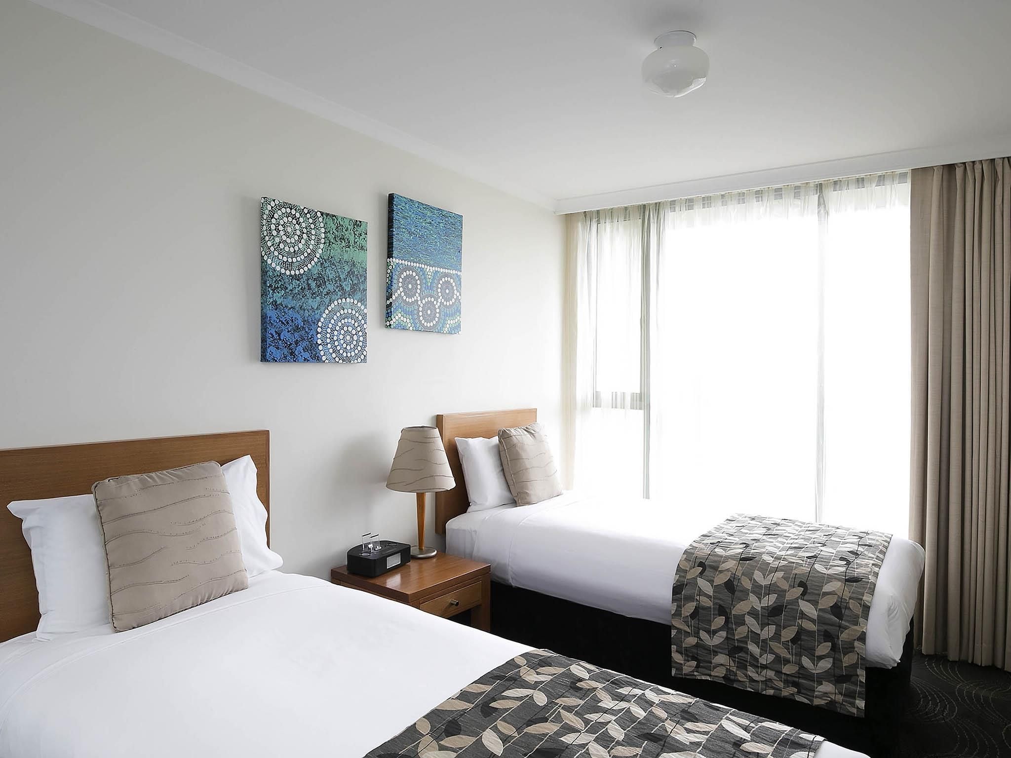 Una habitación de hotel con dos camas, una mesita de noche con lámpara y una obra de arte en la pared.