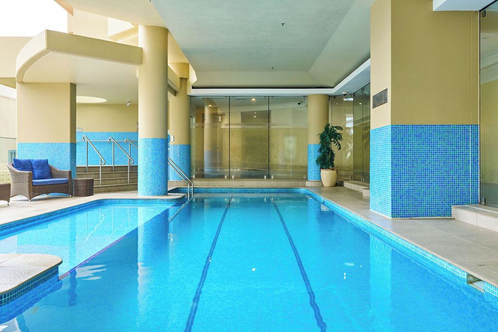 An indoor swimming pool with clear blue water, surrounded by beige walls and blue-tiled steps.