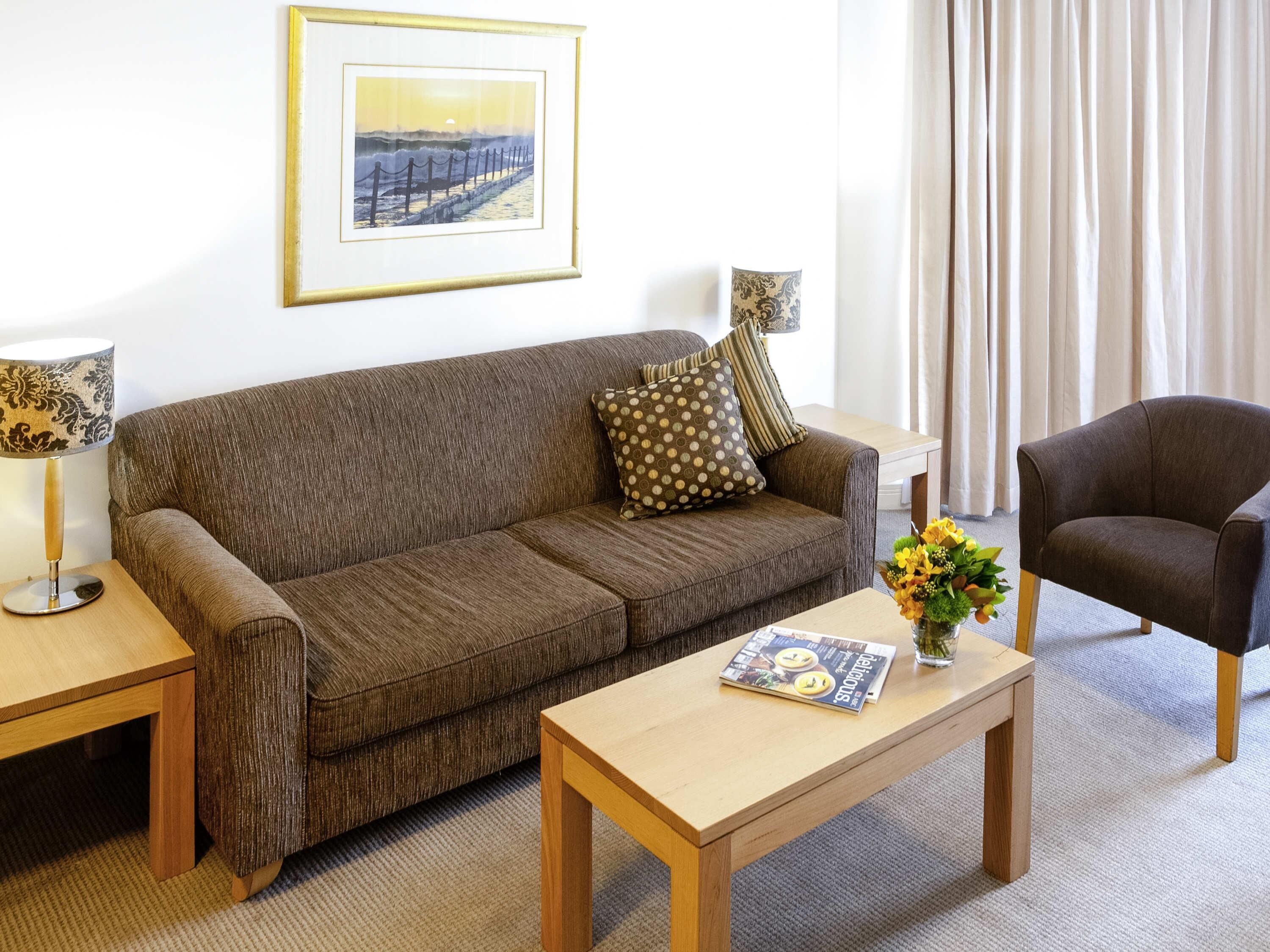 A living room with a brown sofa, a wooden coffee table, a framed picture on the wall, and a chair.