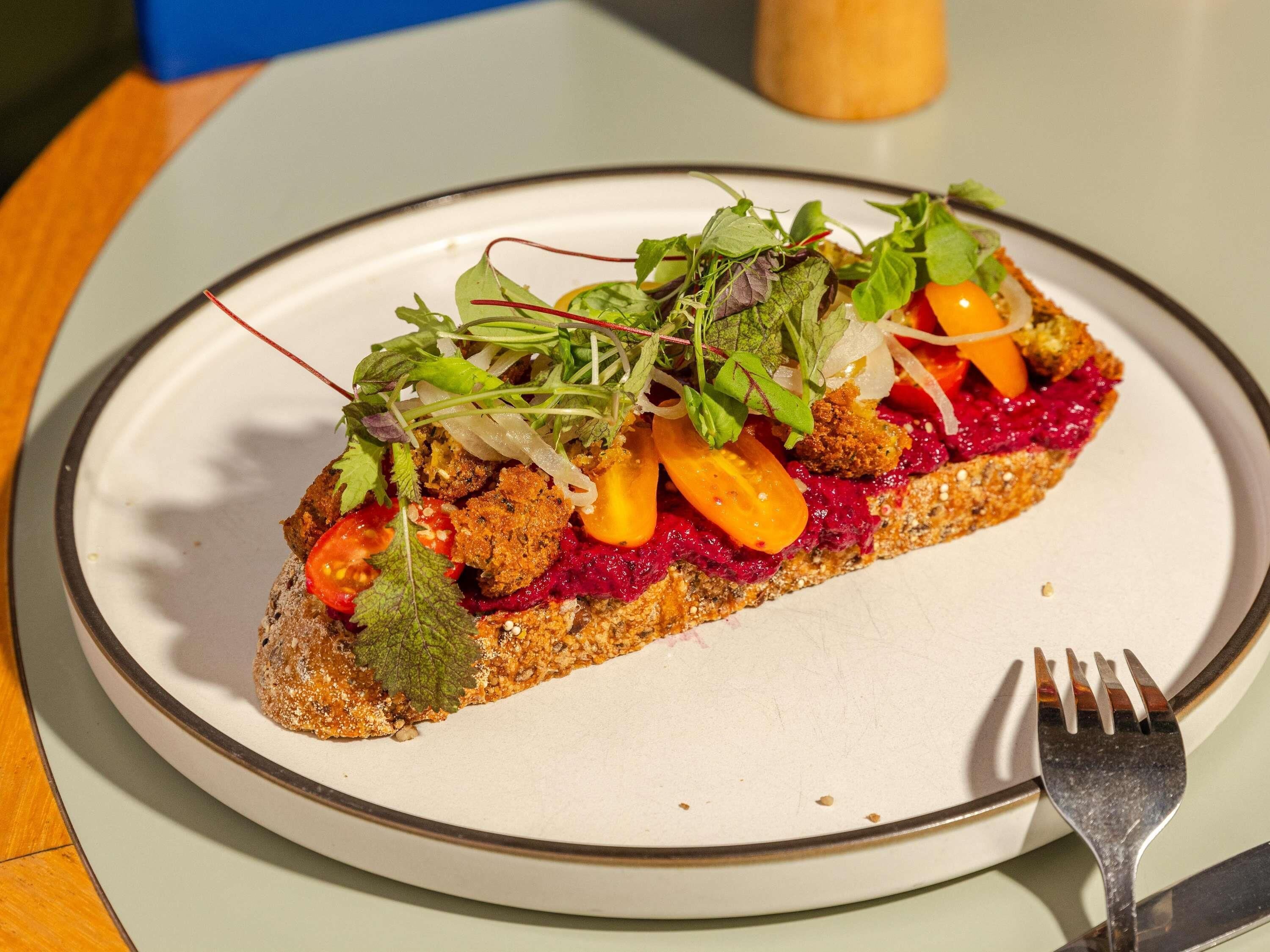 Ein Teller mit einem Sandwich, belegt mit verschiedenen Gemüsesorten und Salat, dazu eine Gabel.