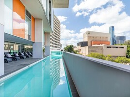 A rooftop pool with lounge chairs, a modern building, and a view of Brisbane's skyline.