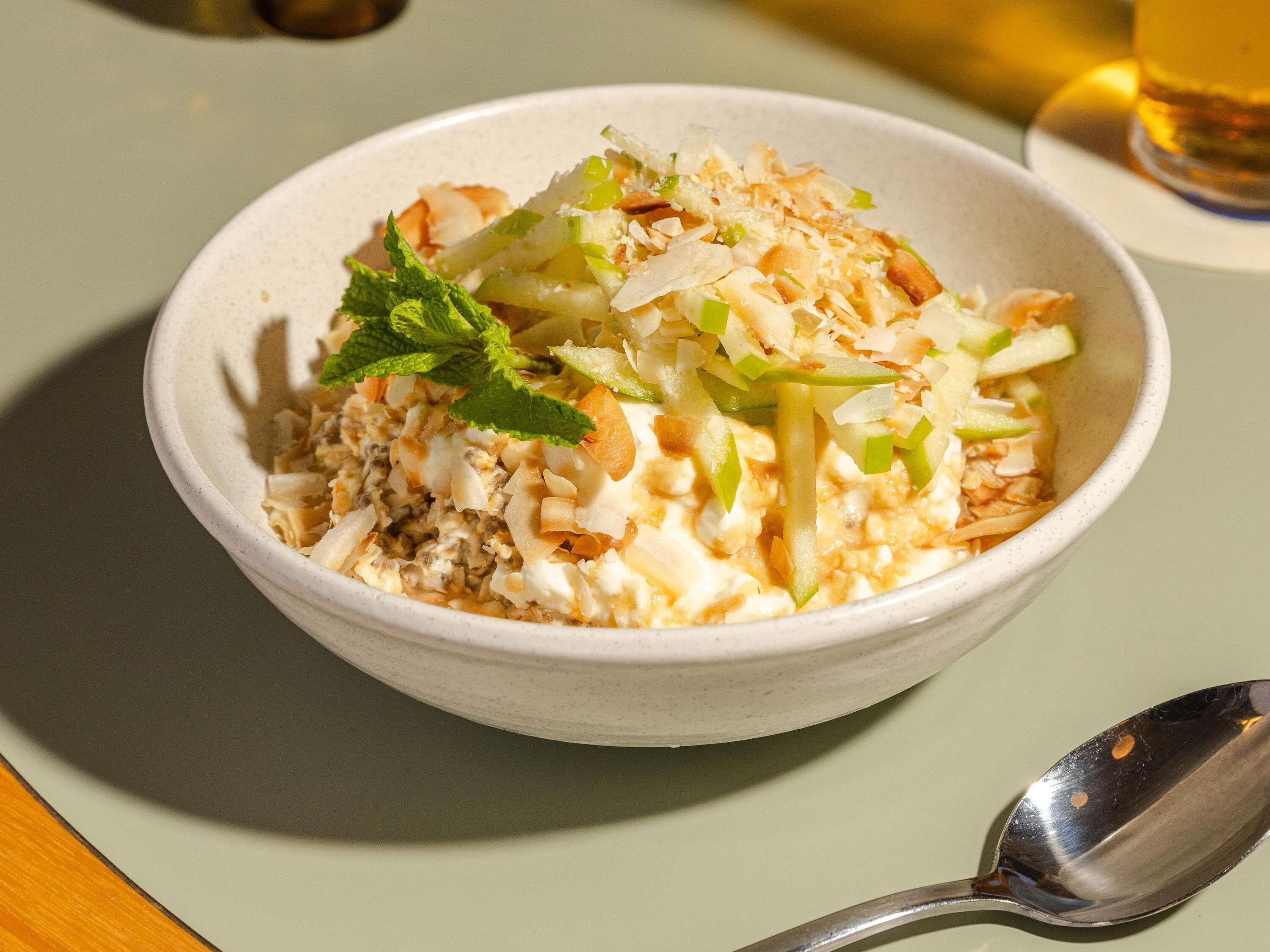 A bowl of food with shredded vegetables and a mint garnish on a table.