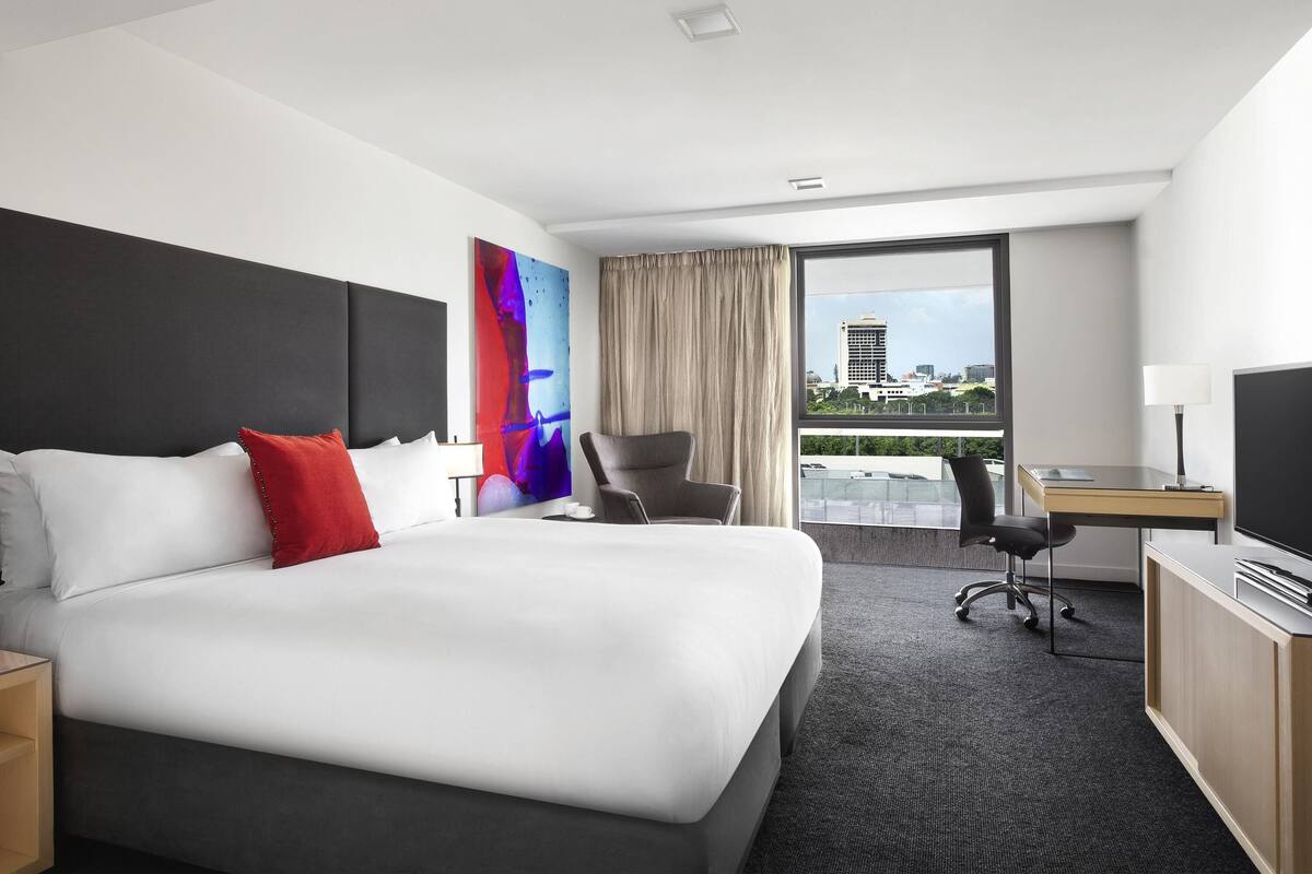 A hotel room with a large bed, a desk, a chair, and a view of the city.