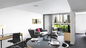 A modern hotel room with a dining area, a sofa, and a view of the cityscape.