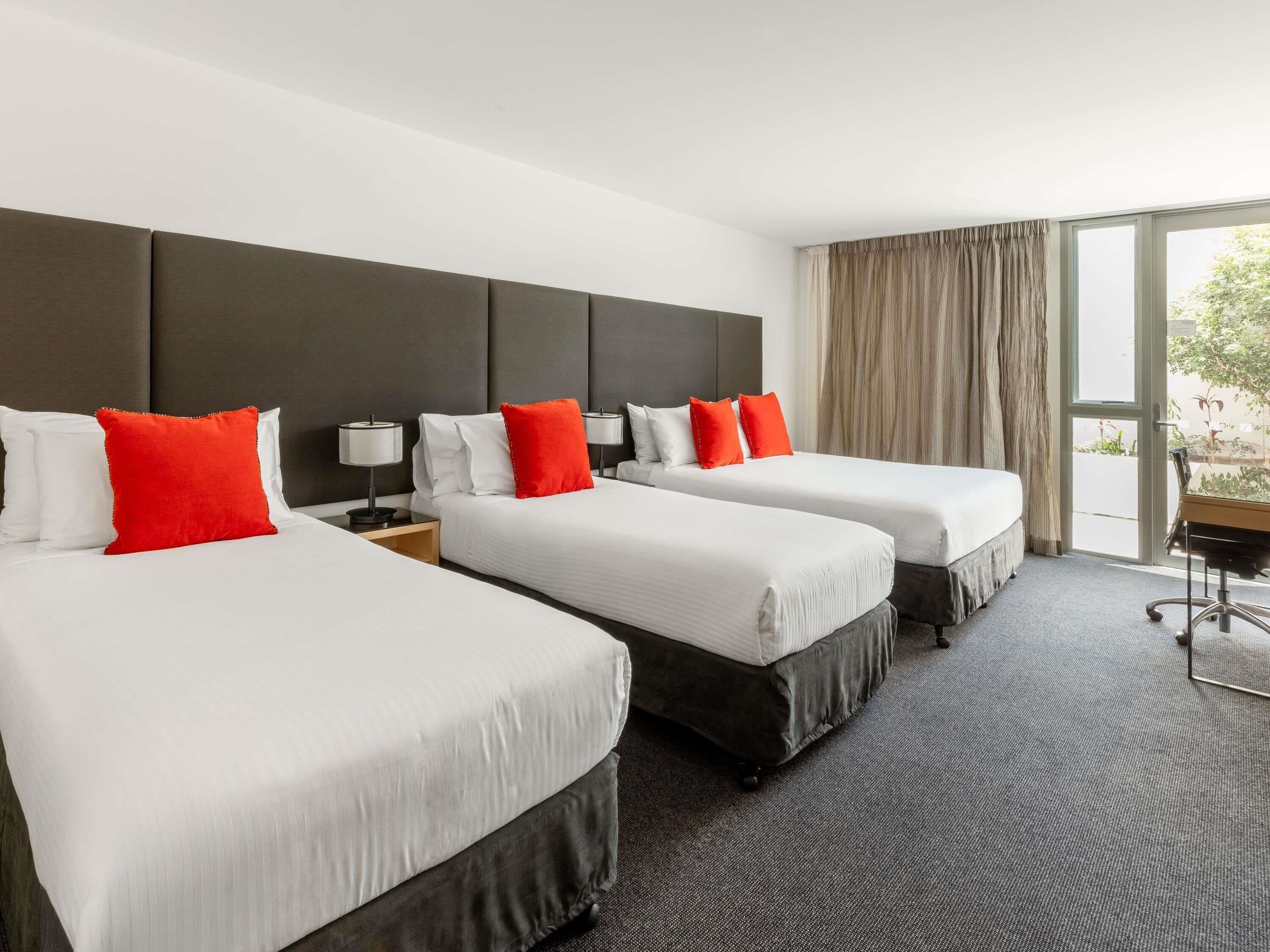 A hotel room with two beds, a desk, and a large window.