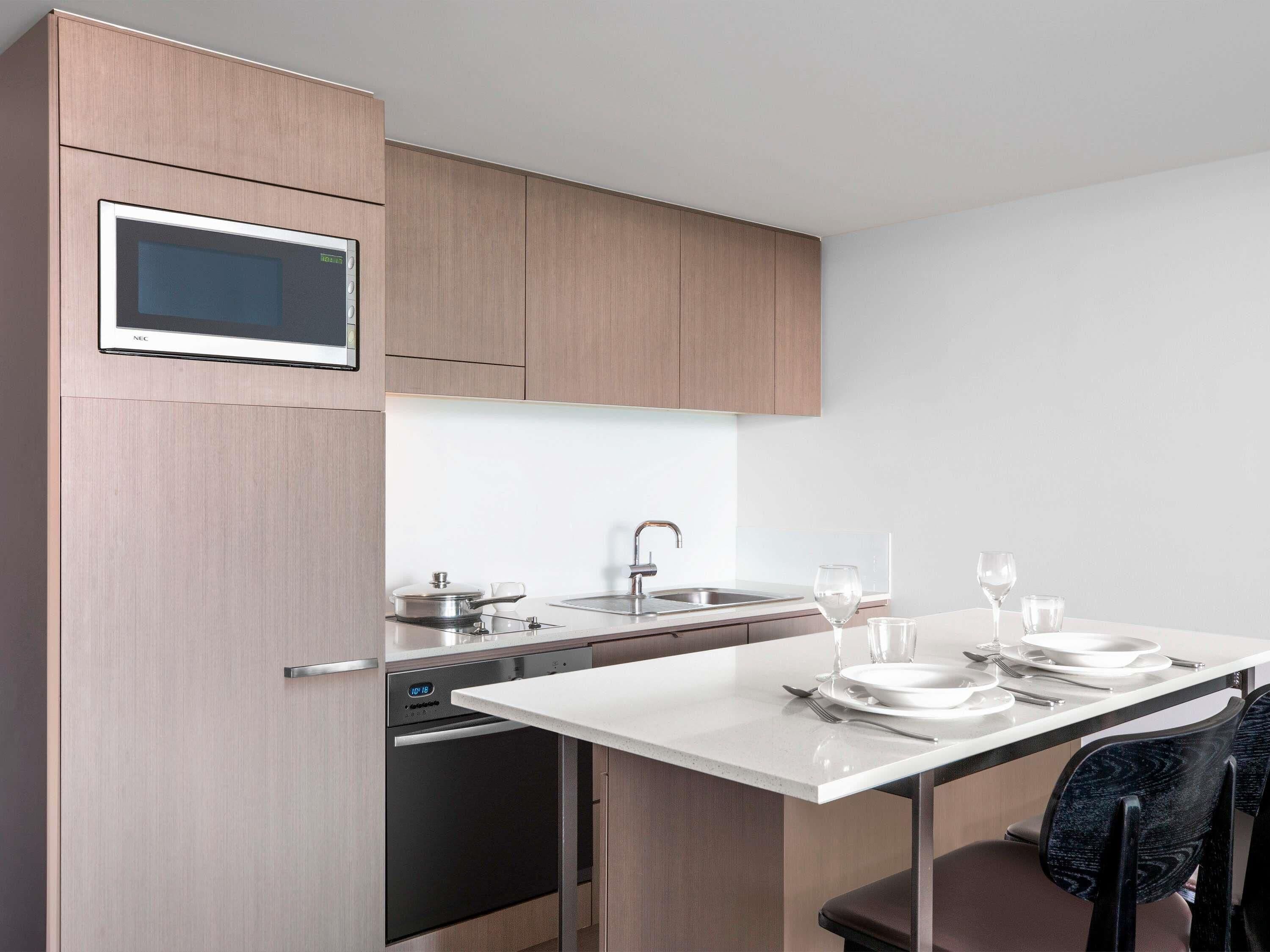 A modern kitchen with a built-in microwave, a dishwasher, and a dining area set with plates, glasses, and cutlery.