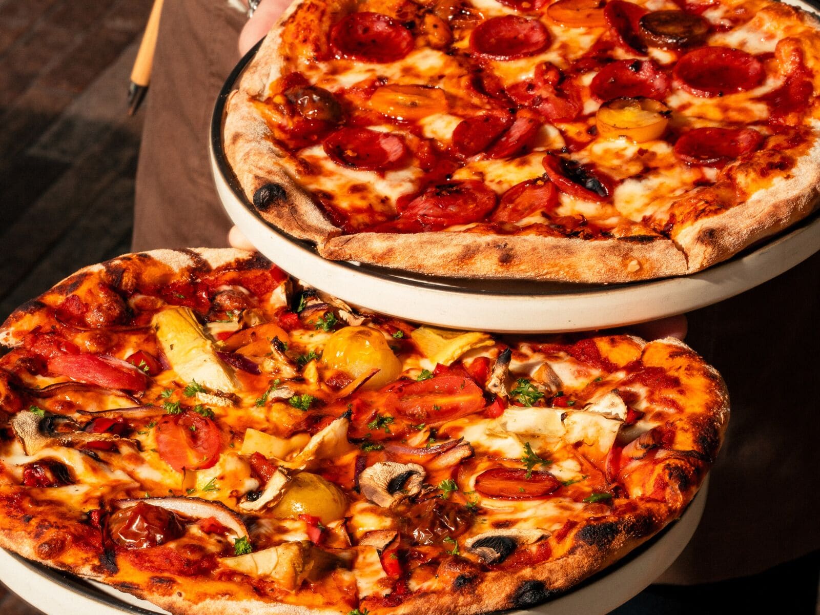 Dos pizzas con diferentes ingredientes sobre platos blancos.