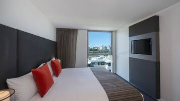Une chambre d’hôtel avec un grand lit, un téléviseur fixé au mur et une vue sur la ville grâce à une grande fenêtre.