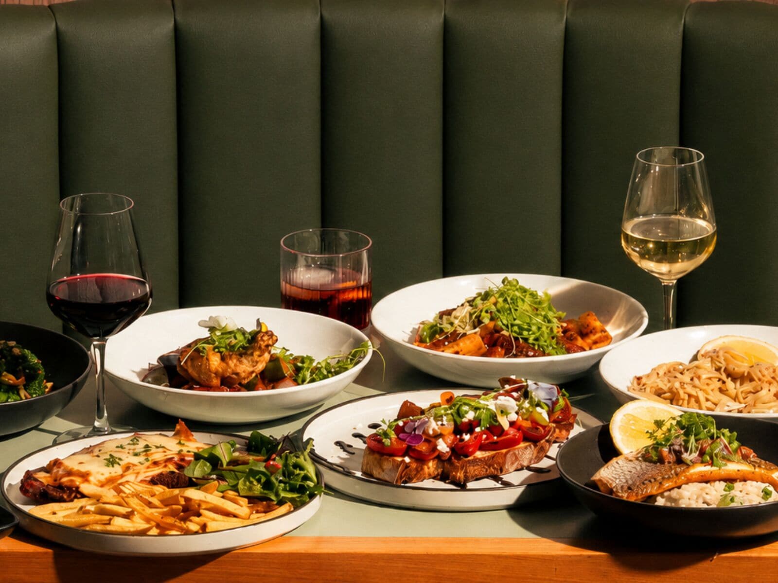 A dining table with multiple plates of food and glasses of wine.