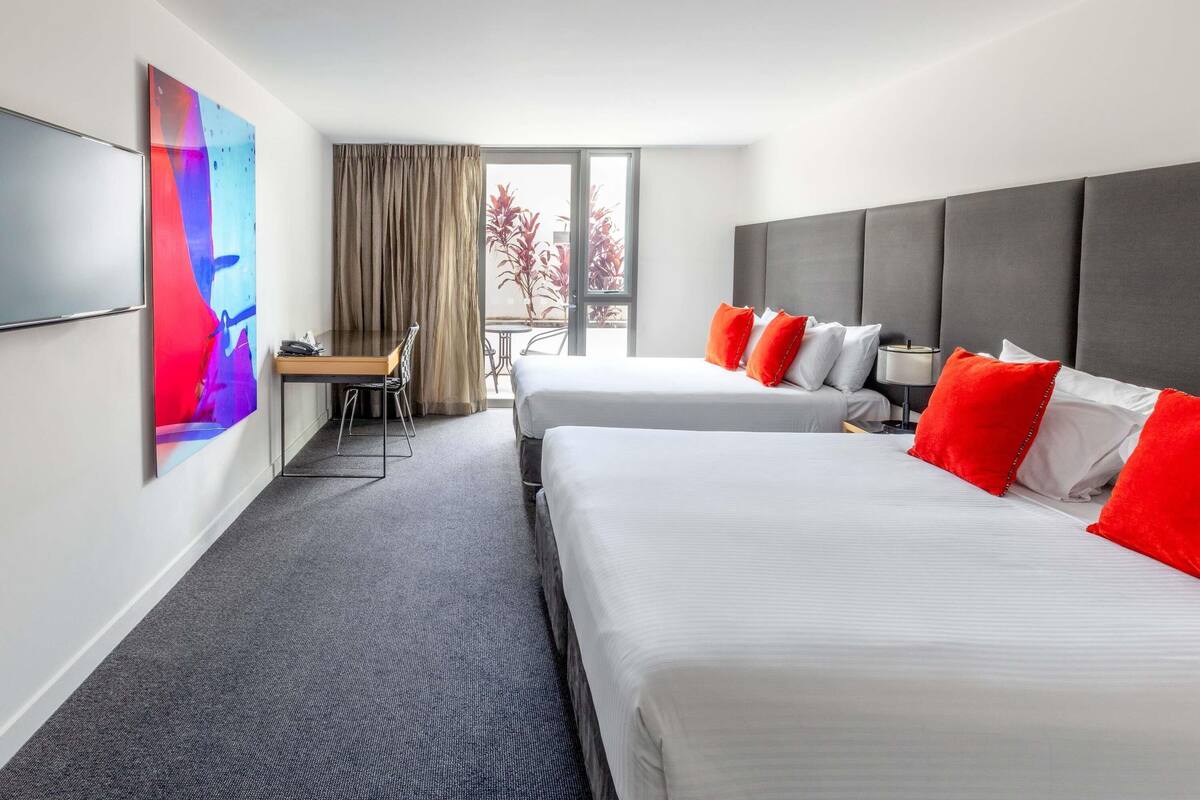 A hotel room with two beds, a desk, a chair, a TV, and a balcony with a view.