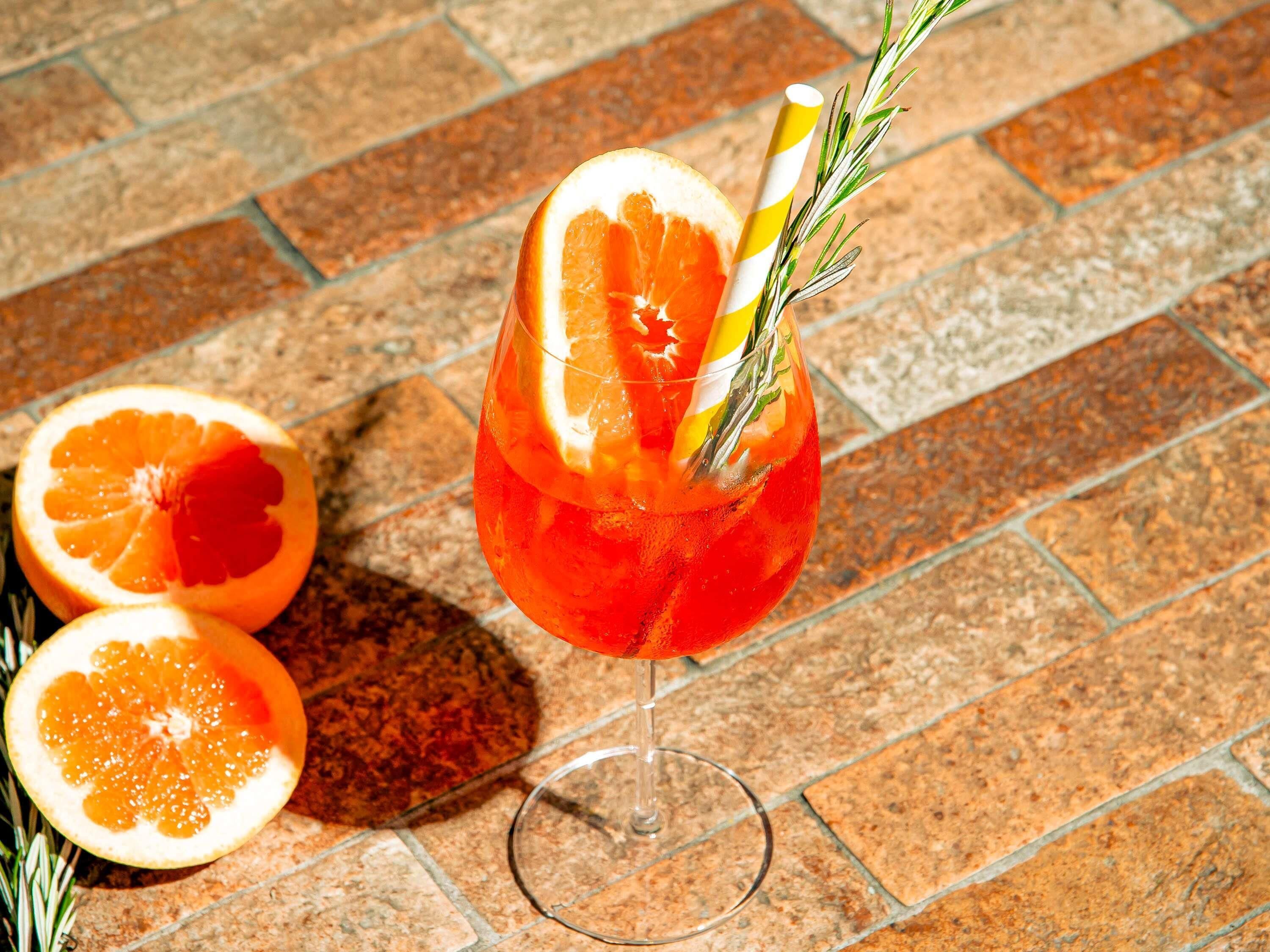 Ein Glas mit einem Getränk, eine halbe Orange und ein Rosmarinzweig auf einer gefliesten Oberfläche.