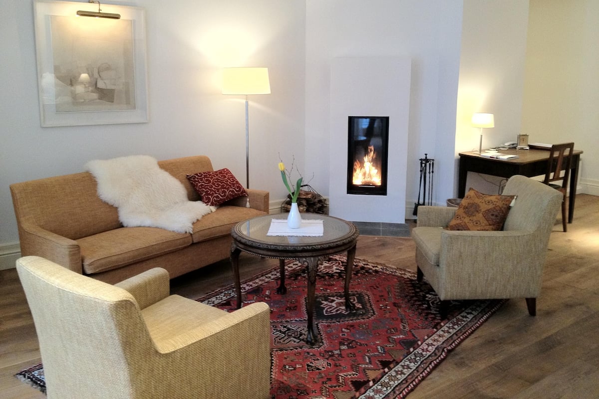 A living room with a sofa, armchairs, a coffee table, a fireplace, and a dining area.