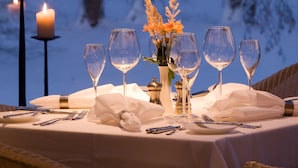Ein gedeckter Tisch mit Kerzen, Weingläsern und einem Blumenstrauß, mit Blick auf eine verschneite Landschaft.