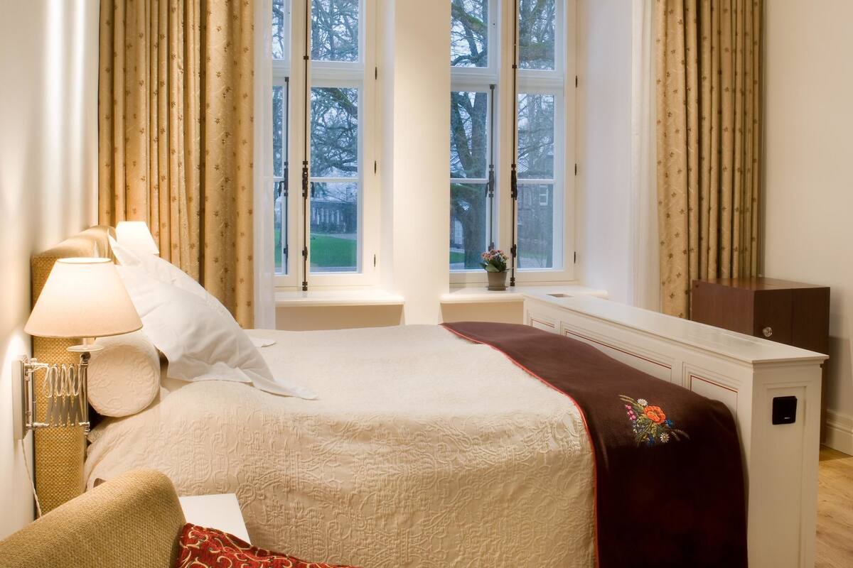 A bedroom with a bed, a chair, a desk, and a window with curtains.