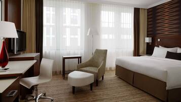 Una habitación de hotel con una cama, un escritorio con televisor, una silla, una lámpara y una ventana con cortinas.