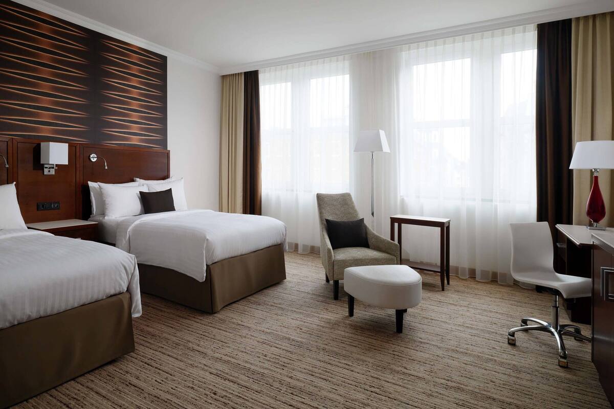 Hotellihuone, jossa on kaksi sänkyä, työpöytä, tuoli ja pieni pöytä.