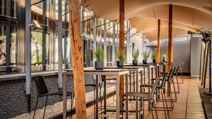 A modern outdoor seating area with tables and chairs, potted plants, and a view of a building with large windows. - Cologne Marriott Hotel (Cologne)