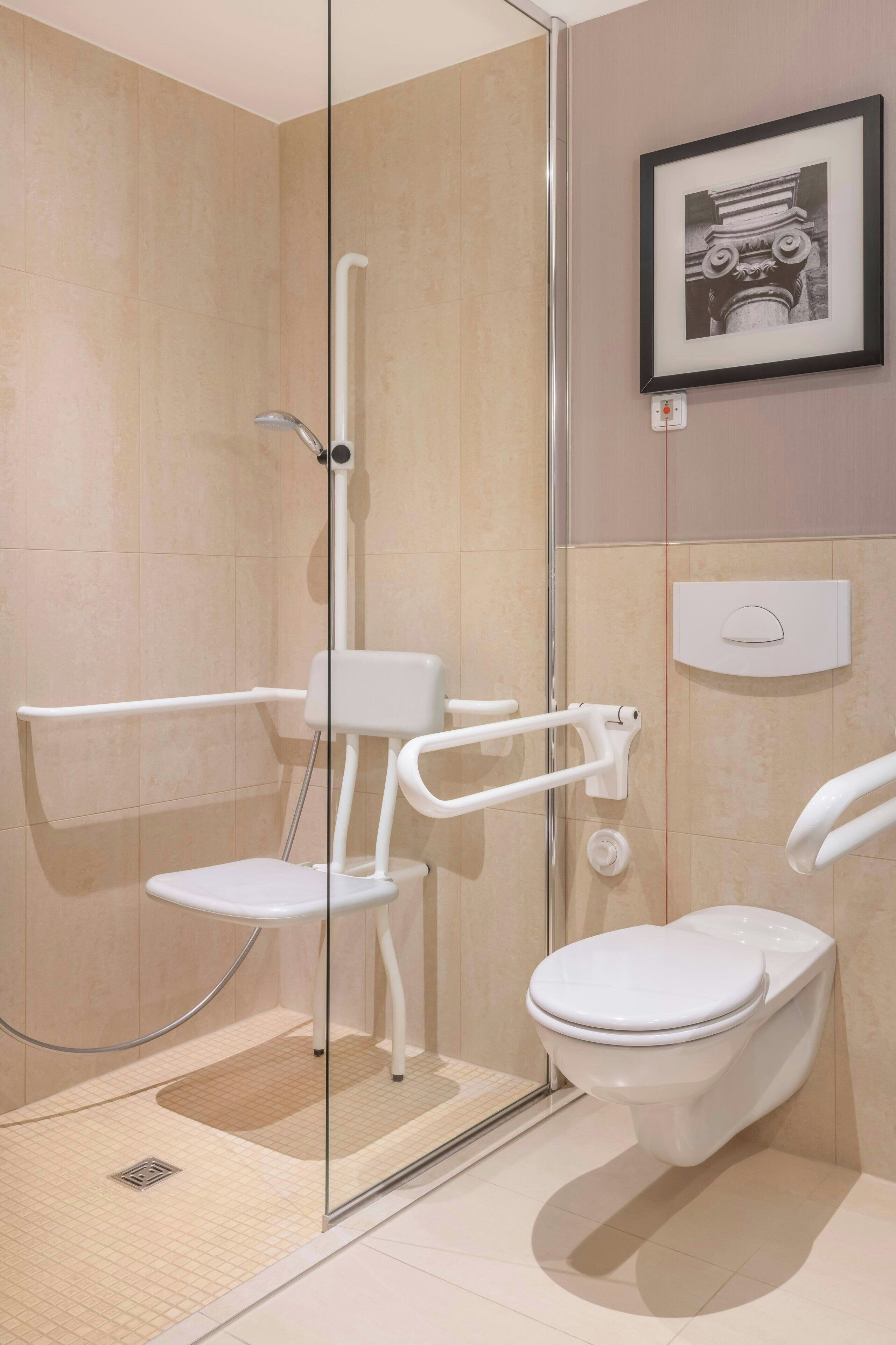 Un baño moderno con ducha de vidrio, inodoro blanco y barra de apoyo para accesibilidad.