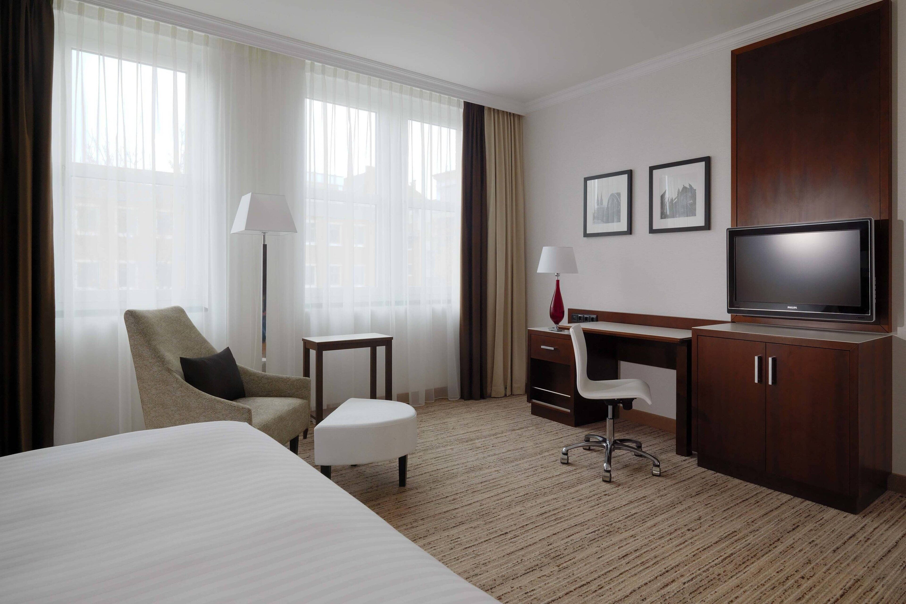 A hotel room with a bed, a desk, a chair, a television, and a window with curtains.