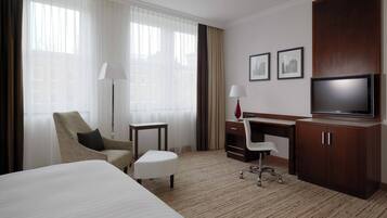 A hotel room with a bed, a desk, a chair, a television, and a window with curtains.