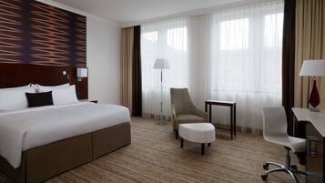 A hotel room with a large bed, a desk, a chair, and a small table.