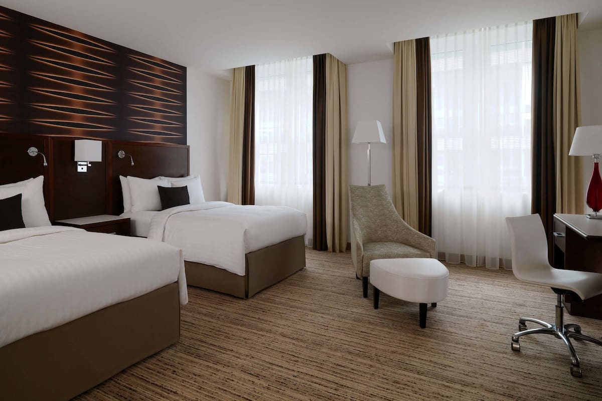 Hotellihuone, jossa on kaksi sänkyä, työpöytä, tuoli ja lamppu.