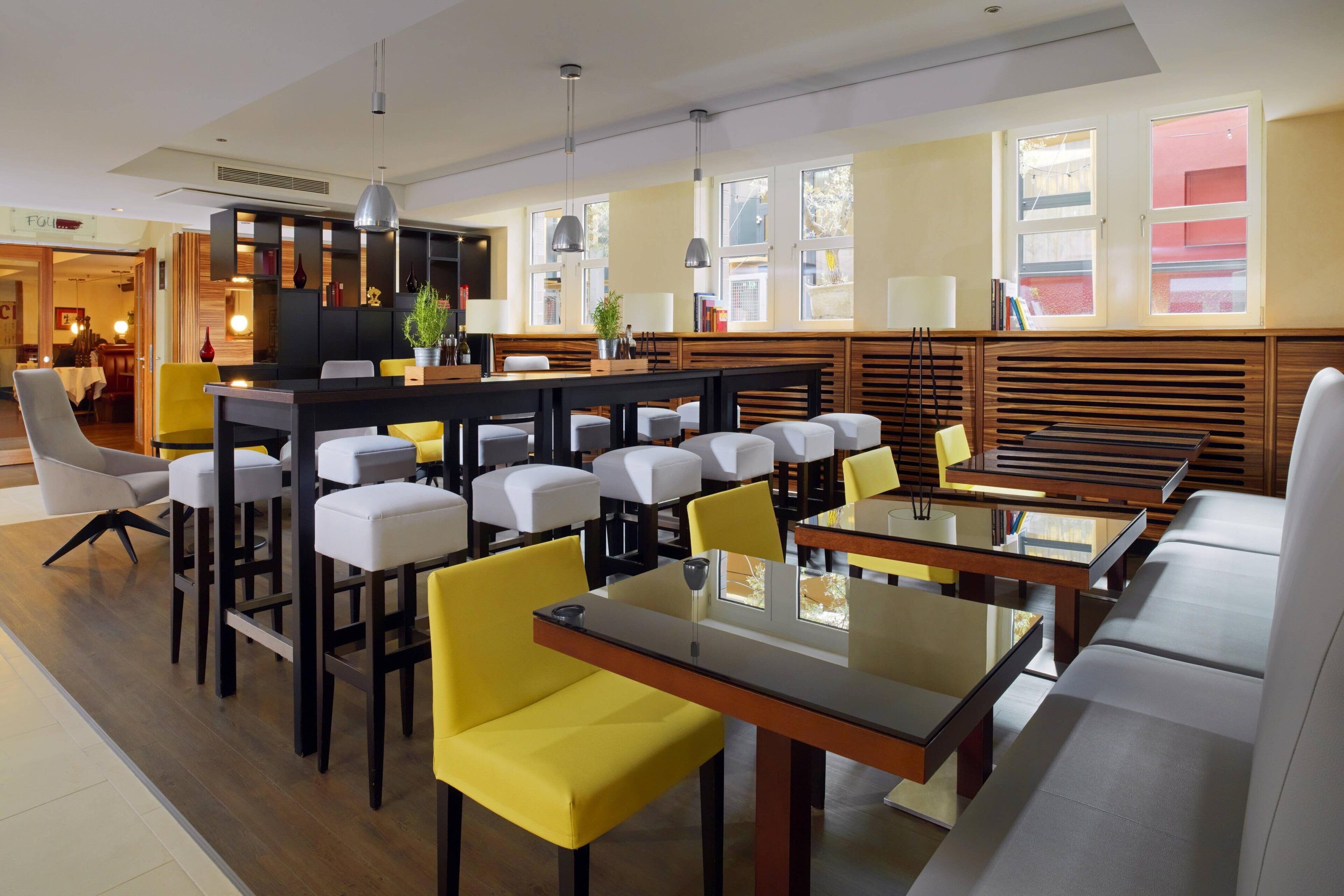 A modern restaurant with multiple seating areas, including booths and high tables, and a bar area with a counter and stools.
