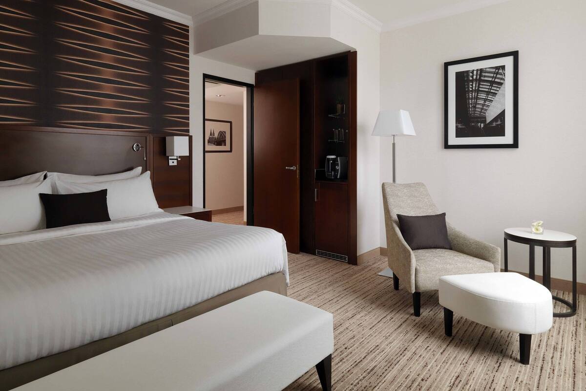 Hotellihuone, jossa on suuri sänky, tuoli, pieni pöytä ja seinällä kehystetty kuva.