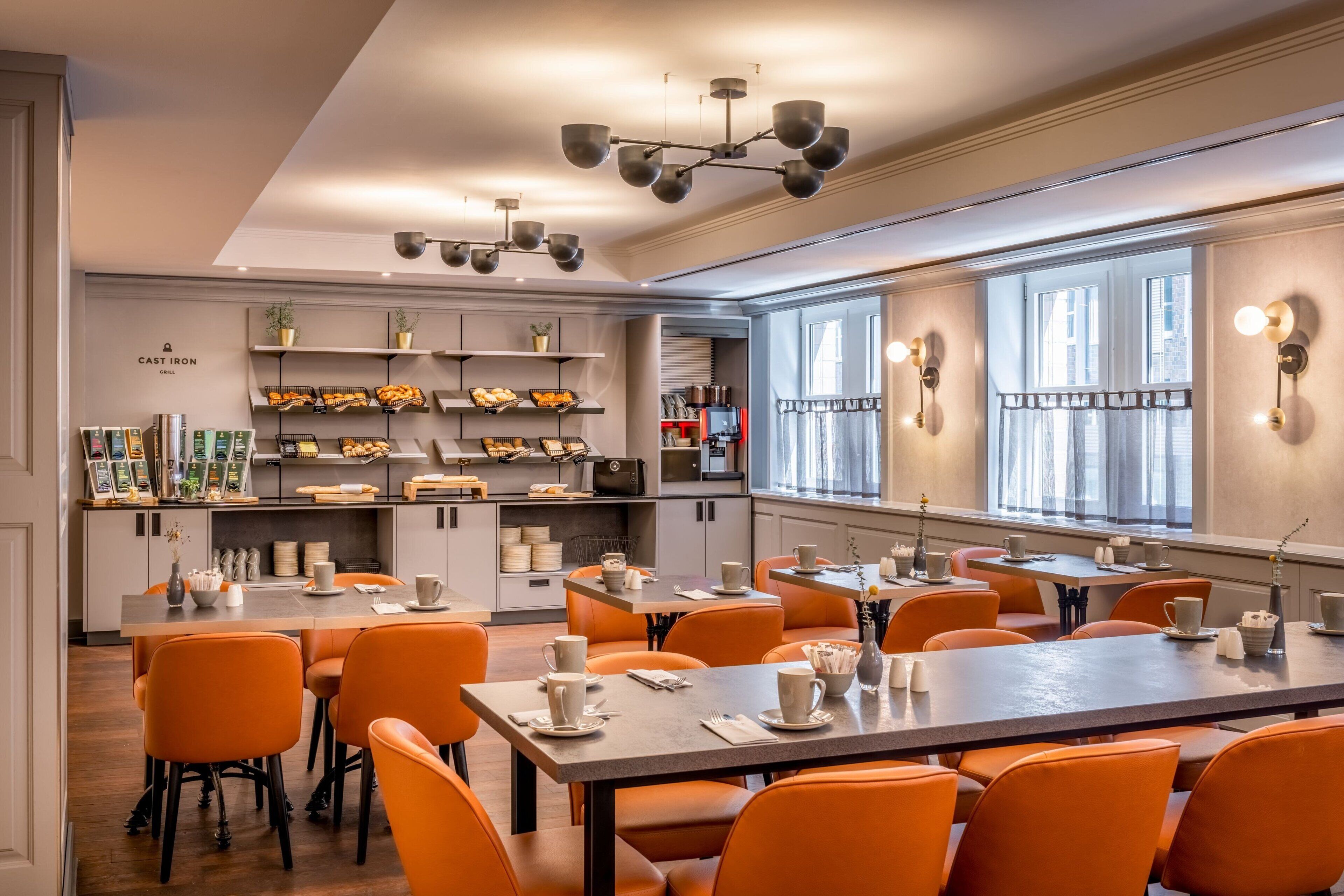 Un comedor moderno con sillas naranjas, una mesa larga y una zona de cocina con estantes y electrodomésticos.