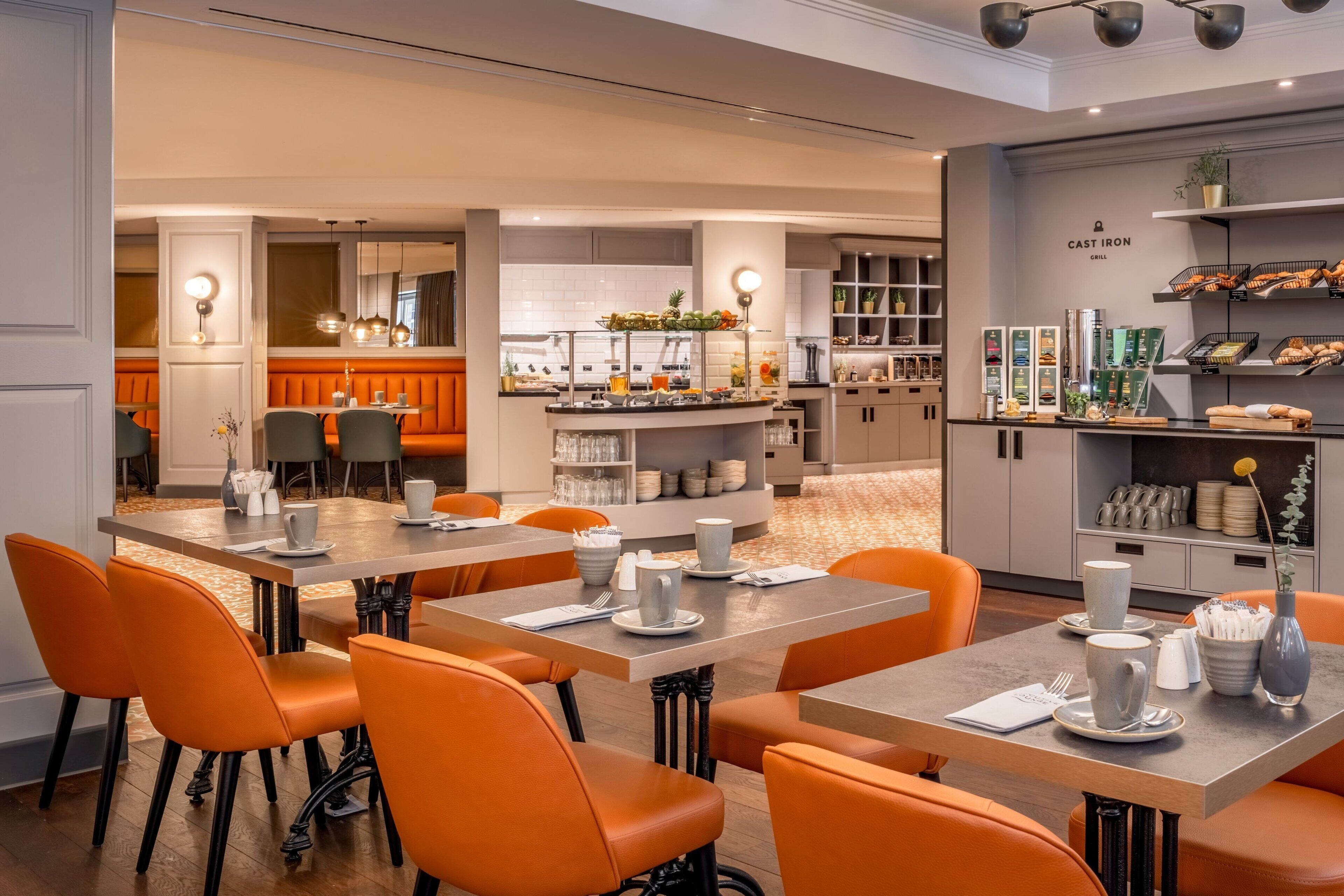 Een modern restaurant met oranje zitplaatsen, een bar en een presentatie van eten en drinken.