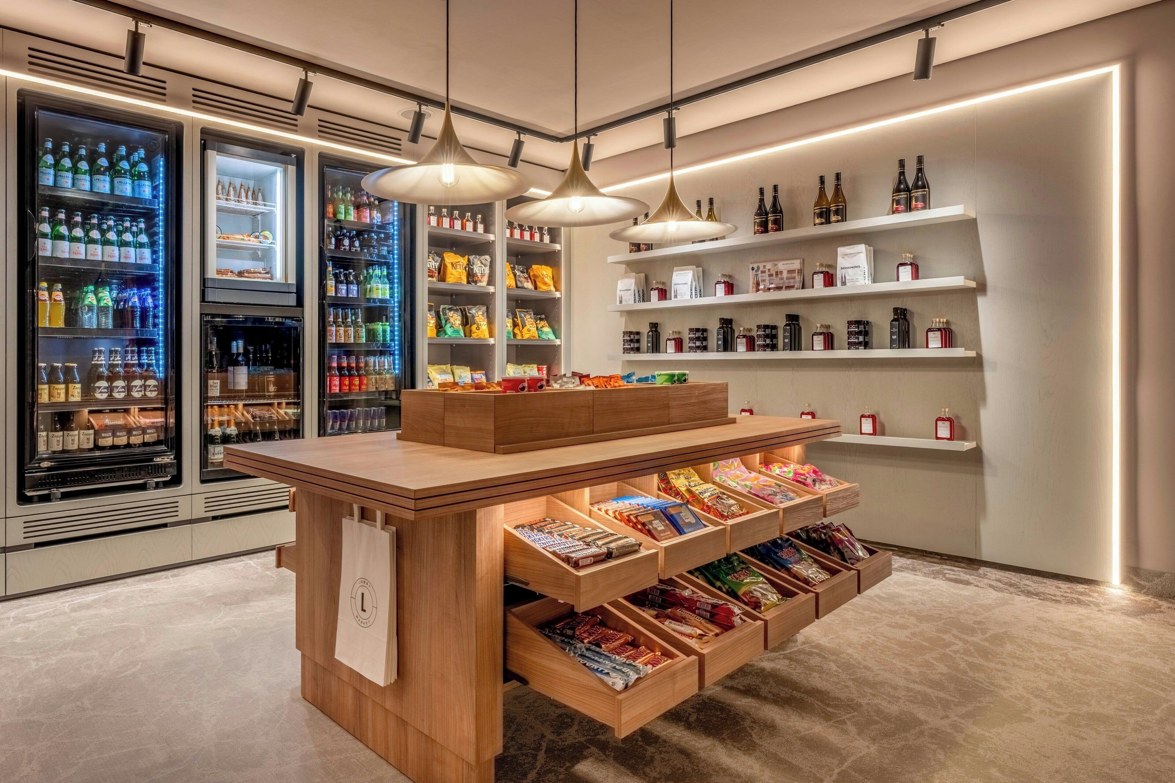 A modern retail space with refrigerated beverage displays, snack shelves, and a wooden counter with drawers.